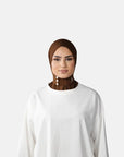 Woman wearing a brown hijab and white outfit against a gray background