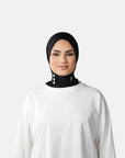 Woman wearing a black hijab and white outfit against a gray background