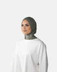 Woman wearing a green hijab and white outfit on a gray background