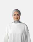 Woman wearing a gray hijab and white outfit against a gray background