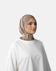 Woman wearing a beige hijab and white shirt against a gray background