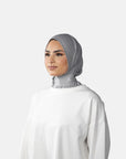 Woman wearing a gray hijab and white top against a gray background