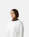 Woman wearing a brown hijab and white top against a gray background
