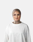 Woman wearing a beige hijab and white shirt against a gray background