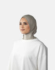 Woman wearing a beige hijab and white outfit on a gray background