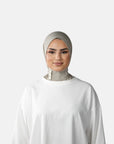 Woman wearing a white outfit and headscarf against a gray background