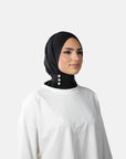Woman wearing a black hijab and white top on a gray background